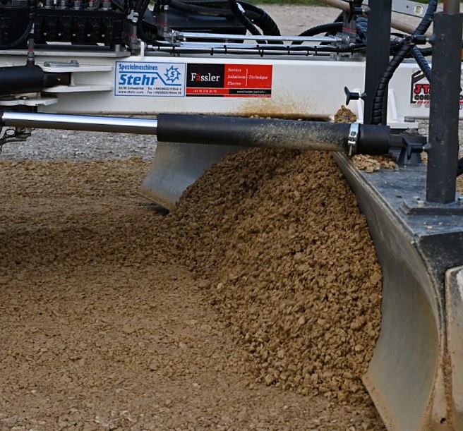The grading blade pushing material, with the Stehr and Fässler logos visible